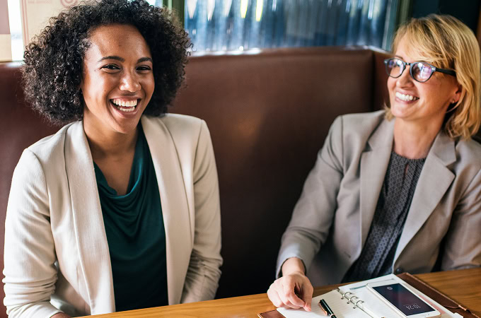 Two businesswomen smiling and talking at a table, having a meeting. Business professionals collaborating in a cafe.