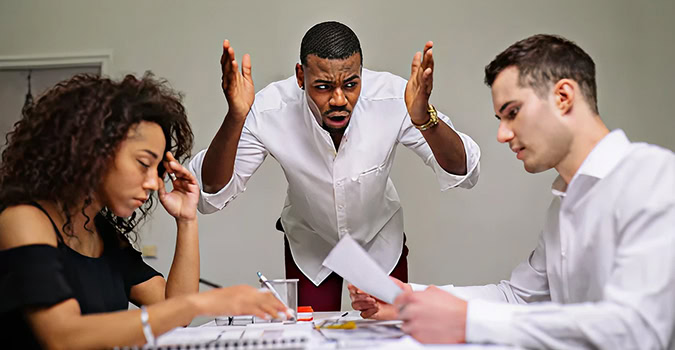 Frustrated businessman gestures at meeting with stressed colleagues. Teamwork, business conflict, and deadline pressure concept.