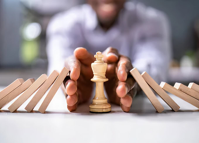 Hands stopping domino effect with chess king. Strategy, risk management, and business protection concept.