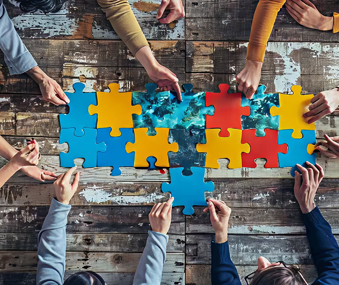 Teamwork puzzle concept: Many hands connecting colorful jigsaw pieces on a rustic wooden surface, symbolizing collaboration.