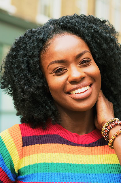 Smiling Black woman with curly hair wearing rainbow sweater and beaded bracelets. Portrait of cheerful African American woman.